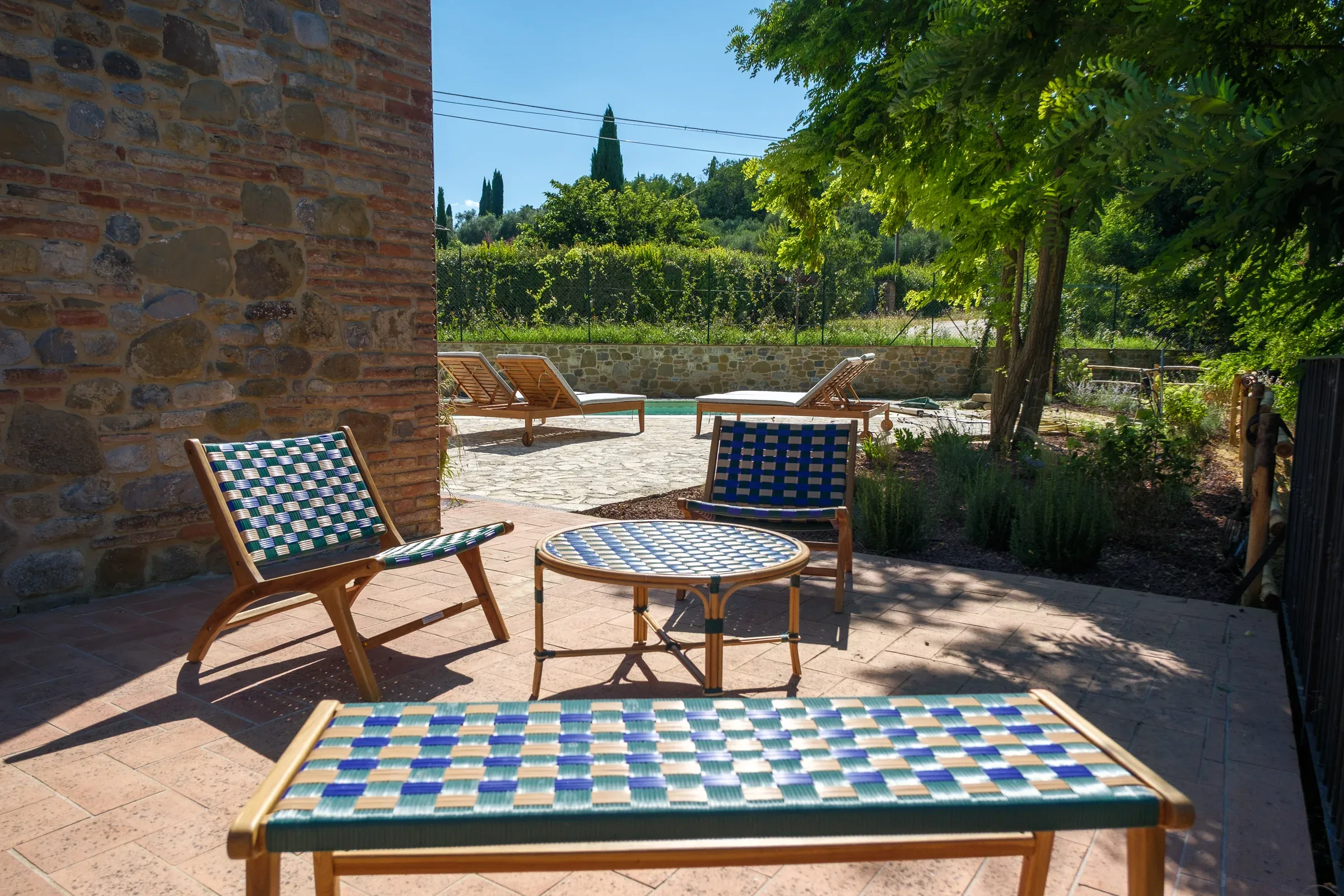 Woven armchairs and bench in the shade, next to the pool