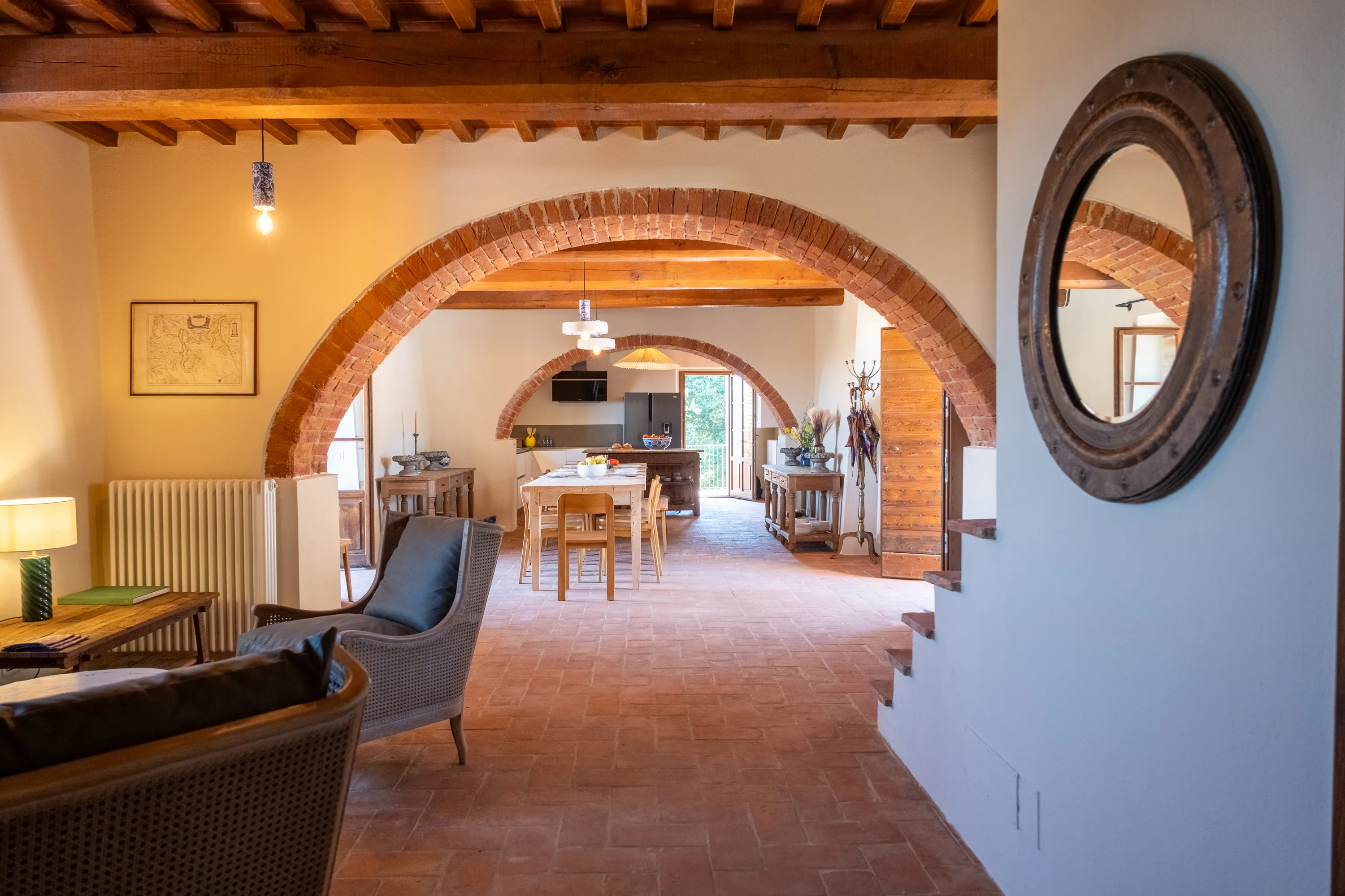 Soggiorno sotto gli archi in mattoni con poltrone e sala da pranzo